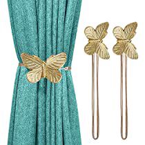 two gold butterfly hair pins sitting on top of a green curtain next to a pair of blue curtains