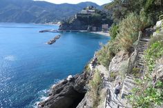 people are walking along the edge of a cliff by the ocean with stairs leading up to it