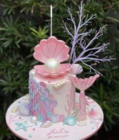 a pink and purple cake decorated with pearls, seashells and mermaid tail decorations