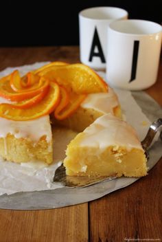 a piece of cake with icing and oranges on it next to a cup