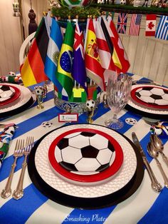 a table set with plates, silverware and soccer themed napkins in front of flags