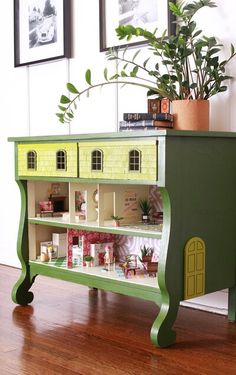 a toy house on top of a book shelf with plants in the corner next to it