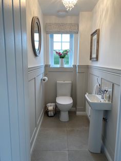 a white toilet sitting next to a sink in a bathroom under a window with a mirror above it