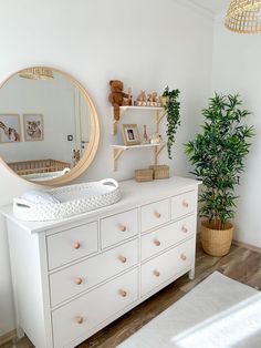 a baby's room with a dresser, mirror and potted plant in the corner