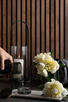 a person pouring water into a glass on a tray with flowers and cookies next to it