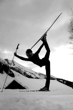 a woman standing on one leg while holding skis in the air with both hands