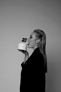 a woman is eating a cake with the number twenty five on it while standing in front of a gray wall