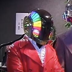 a man in a red leather jacket wearing a rainbow colored helmet and standing next to another man