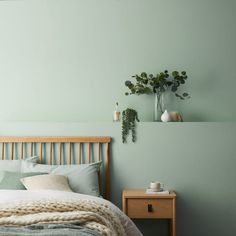 a bedroom with green walls and a wooden headboard on the bed, next to a small table with a potted plant