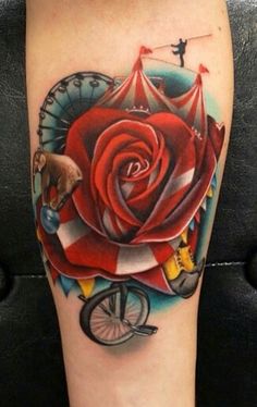 a rose tattoo on the leg with a bicycle and circus tent in the back ground