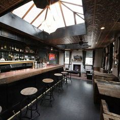 an empty bar with stools and tables in front of the bar area, under a skylight