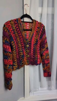 a colorful crocheted sweater hanging on a hanger in front of a window