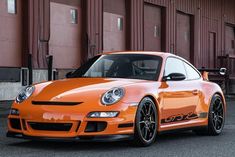 an orange porsche sports car parked in front of a red building with black rims