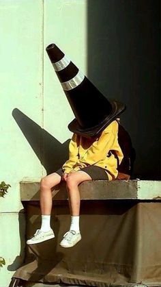 a young boy wearing a black and white hat sitting on top of a cement block