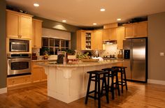 a large kitchen with wooden floors and stainless steel appliances, along with two bar stools