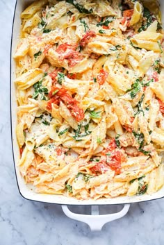 baked fettuccine with tomatoes and spinach in a white casserole dish