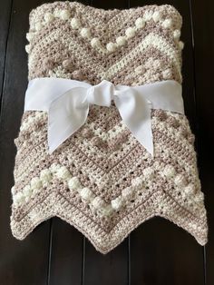 a crocheted blanket with a white bow on the front and back, sitting on top of a wooden floor