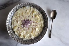 a bowl of oatmeal sits next to a spoon on a marble table