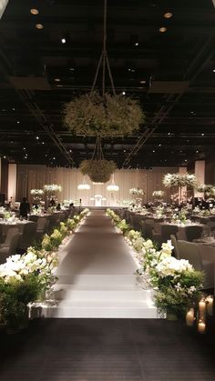 an indoor wedding venue with white flowers and greenery on the aisle, chandeliers hanging from the ceiling