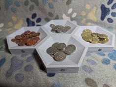 three hexagonal boxes filled with coins sitting on top of a floral print blanket