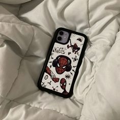 a spiderman phone case sitting on top of a white bed sheet with other things around it