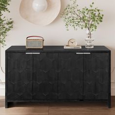 a black sideboard with a hat on top and plants in vases next to it