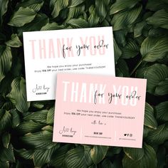 two pink and white thank you cards on top of some green leaves in the background