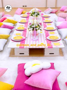 a table set up with pink and yellow pillows, plates and napkins on it