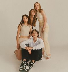 three women and one man posing for a photo with their arms around each other in front of a white background