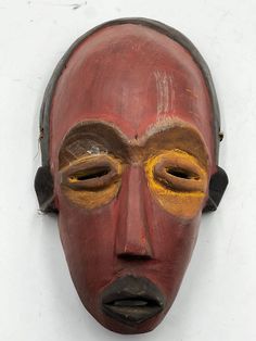 a red mask with yellow eyes on a white wall