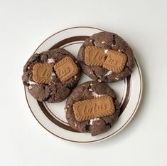 three chocolate cookies with peanut butter on top are sitting on a brown and white plate