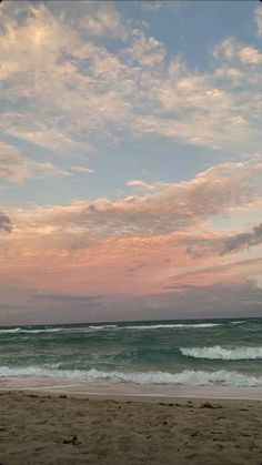 a person walking on the beach with a surfboard under their arm, and clouds in the background