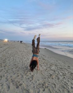 a person doing a handstand on the beach with their feet in the air