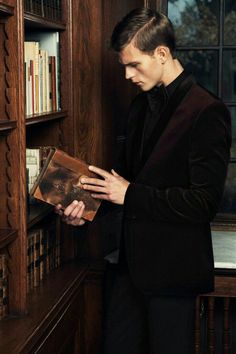 a man in a suit is looking at an open book on a shelf with bookshelves behind him