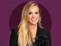 a woman with long blonde hair wearing a black jacket and flower in front of a purple background