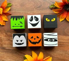 four wooden blocks decorated with halloween faces and pumpkins on a table next to flowers