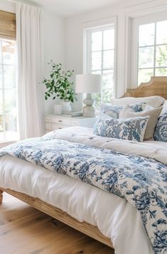 a bed with blue and white comforter in a bedroom next to two large windows