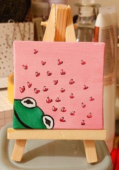 an easel with a painting on it in the shape of a green monster and hearts