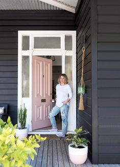 a woman standing in the doorway of a black house with potted cacti