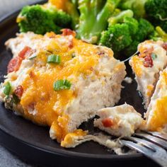 a black plate topped with broccoli and chicken covered in cheesy sauce