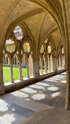 the inside of an old building with stone columns and arches on both sides, looking out onto a grassy area