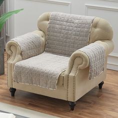 a chair with a blanket on it in front of a potted plant and wooden floor