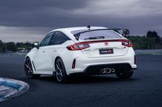 the rear end of a white car on a race track with dark clouds in the background