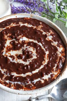 a bowl filled with chocolate and cream on top of a wooden table next to flowers