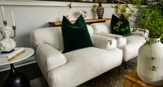 two white couches sitting next to each other with green pillows on top of them