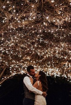 a bride and groom standing under a tree covered in lights