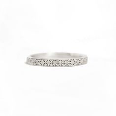 a white gold wedding band with intricate design on the outside, and a diamond set in the middle