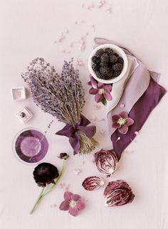 purple flowers and other items on a white table cloth, with petals scattered around them