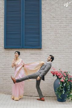 a man and woman dancing in front of a brick building with blue shutters on the windows