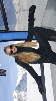 a woman with long blonde hair standing in front of a glass window and looking at the camera